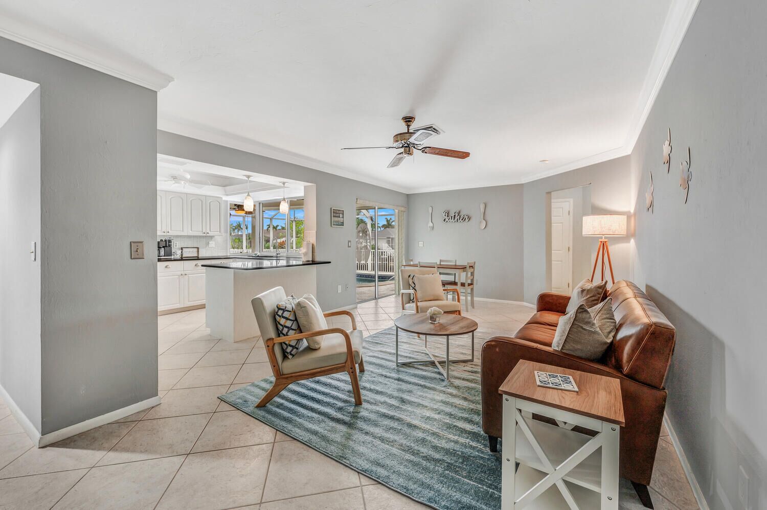 A spacious living area with a sofa, armchair, and coffee table, a kitchen with white cabinets, and a dining area with a table and chairs.