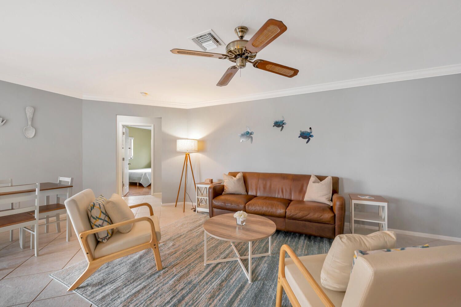 A modern living room with a brown leather sofa, wooden chairs, a coffee table, and a ceiling fan.