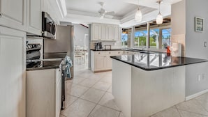 Una cocina moderna con muebles blancos, una isla central y vistas al exterior.
