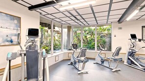 A gym with exercise equipment, large windows, and a view of greenery.
