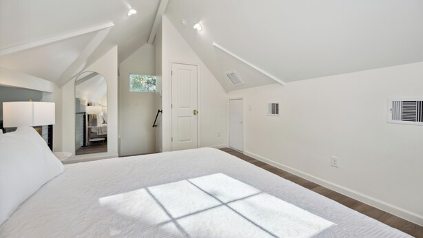 Un dormitorio espacioso con una cama grande, tragaluces y vistas a un pasillo con una puerta y una ventana.