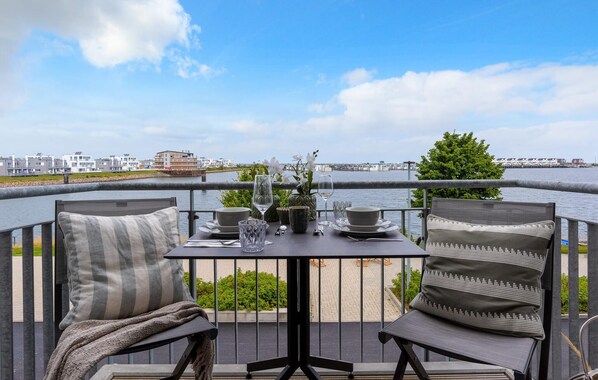 En balkon med et bord dækket til to, med udsigt over en havnefront med bygninger i baggrunden.