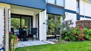 A modern house with a patio, a dining table with chairs, and a garden with pink flowers. - Lille, Wenningstedt-braderup auf Sylt, Deutschland (Wenningstedt-Braderup (Sylt))