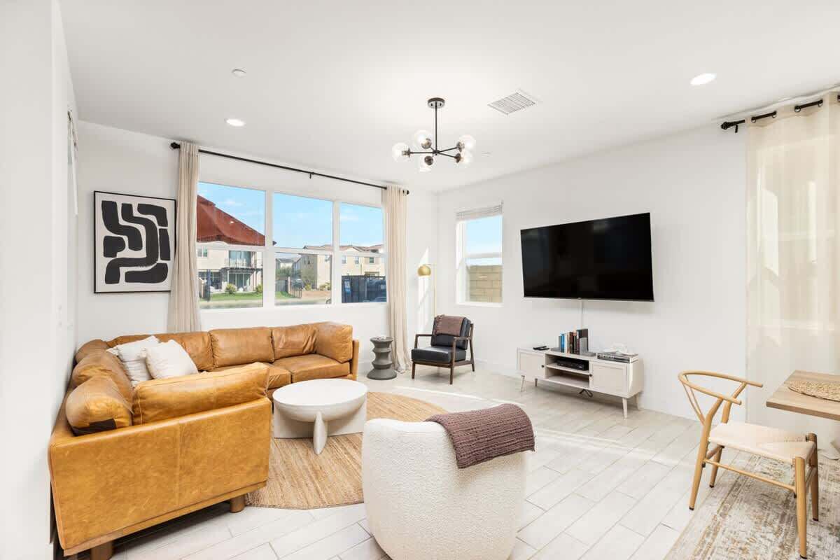 A modern living room with a leather sofa, a white armchair, a coffee table, and a TV mounted on the wall.