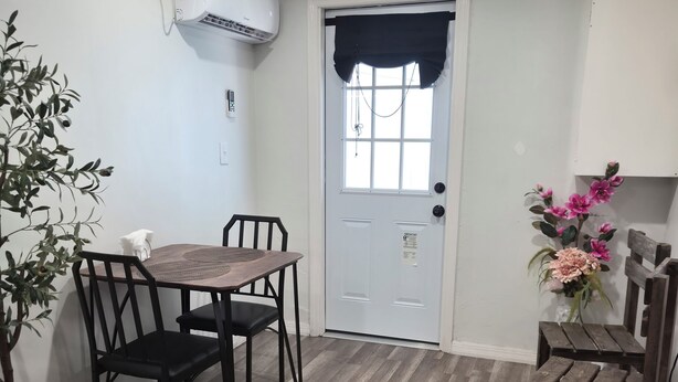 A room with a dining table, chairs, a potted plant, a small wooden table, and a door with a window. - Private & Peaceful Suite | Fast WiFi | Patio | Close to Beaches & Downtown (Port Richey)