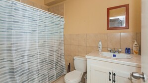 A bathroom with a shower curtain, toilet, sink, and mirror. - Martin's Way@Potters Village 2 BR Apartment (Potters Village)
