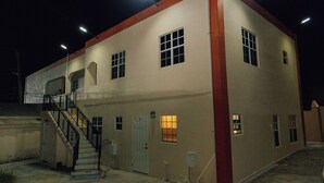 A two-story building with a red accent on the corner, a staircase leading to the upper floor, and a well-lit exterior. - Martin's Way@Potters Village 2 BR Apartment (Potters Village)