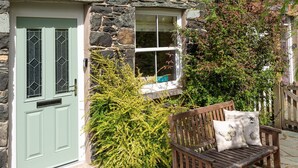 A stone cottage with a green door and a bench outside.