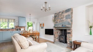 A modern kitchen with light blue cabinets, a dining area with wooden chairs, a beige sofa, and a stone fireplace.