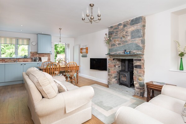 A modern kitchen with light blue cabinets, a dining area with wooden chairs, a beige sofa, and a stone fireplace.