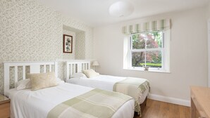 A bedroom with two beds, a window with a view of trees, and a wall with a leafy pattern.