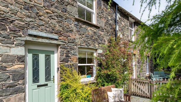 A stone cottage with a green door and a bench outside.
