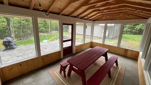 Une terrasse couverte avec une table et des bancs en bois, de grandes fenêtres et une terrasse en pierre à l’extérieur.