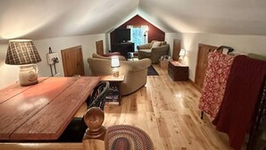 Une pièce mansardée chaleureuse, avec une table en bois, deux chaises, un canapé et un téléviseur en arrière-plan.