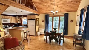 L’intérieur chaleureux d’un chalet avec un plafond en bois, un coin cuisine, une table à manger et un canapé.