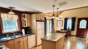 Une cuisine avec des meubles en bois, un îlot central, un réfrigérateur et un coin repas comprenant une table et des chaises.