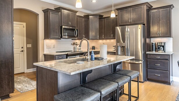 A modern kitchen with dark wood cabinets, stainless steel appliances, and a central island with bar stools. - Mulligan Manor- 0.2 mile walk to Vitos Ristorante and Pizzeria and many others! (Southern Pines)