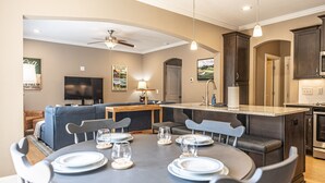 A modern kitchen with dark cabinets, a central island, and a dining area with a round table set for six. - Mulligan Manor- 0.2 mile walk to Vitos Ristorante and Pizzeria and many others! (Southern Pines)