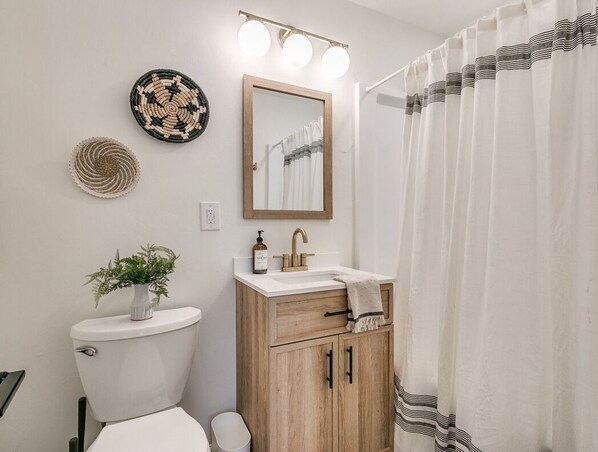 A bathroom with a toilet, sink, mirror, and shower curtain. - The Cali - 1/4 mile to OU Stadium (Norman)