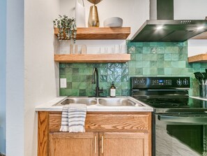 A kitchen with wooden cabinets, a double sink, a stove, and a green tiled backsplash. - The Cali - 1/4 mile to OU Stadium (Norman)