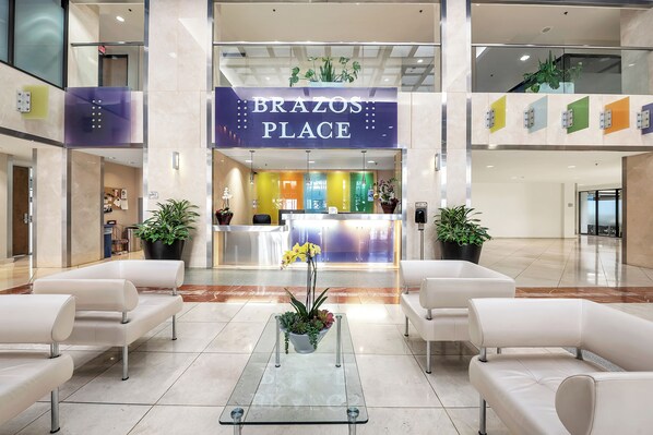 Welcome to the lobby of Brazos Place, where a warm and inviting atmosphere awaits, complete with a reception desk, comfortable seating, and lush greenery.