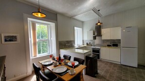 A compact kitchen with white cabinets, a dining table set for four, and a large window providing natural light. - Little Bay View in Oban (Oban)