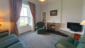 A living room with a fireplace, a television, and a green armchair. - Little Bay View in Oban (Oban)