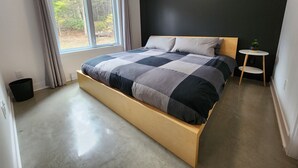 Une chambre à coucher moderne, avec un grand lit, une petite table de chevet et une vue sur les arbres par la fenêtre.