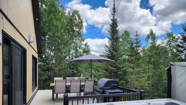 Une terrasse extérieure équipée d’un jacuzzi, d’un barbecue et d’une table avec des chaises.
