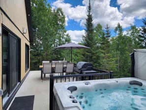 Eine Terrass mit Whirlpool, Grill und Tisch mit Stühlen.