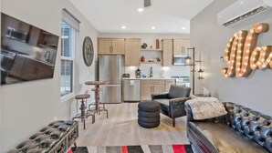 A modern kitchen with stainless steel appliances, a dining area with a black leather sofa and ottoman, and a ceiling fan. - Roof Deck|Pet Friendly|E.Nash (Nashville)