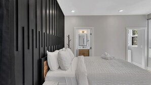 A modern bedroom with a large bed, a dark accent wall, a bathroom with a mirror, and a view of the outdoors. - Roof Deck|Pet Friendly|E.Nash (Nashville)