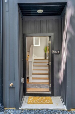 A dark grey door with a "No. 4" sign, a wooden staircase leading inside, and a "hello" mat at the entrance. - Roof Deck|Pet Friendly|E.Nash (Nashville)