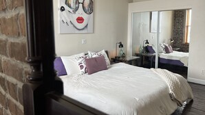 Habitación de hotel con cama, mesita de noche, espejo y una obra de arte con vista a la ciudad.