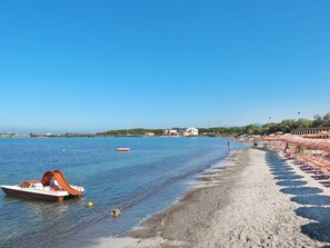Ein Strand mit einer Reihe von Liegestühlen und Sonnenschirmen, einem Boot und einem strahlend blauen Himmel.