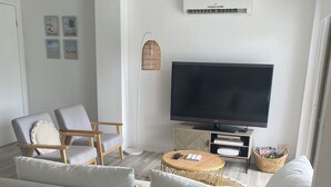 A modern living room with a large flat-screen TV, grey sofas, a round coffee table, and a ceiling fan. - Welcome to our serenity in the Gold Coast which is "Bee Cottage".
 (Robina)