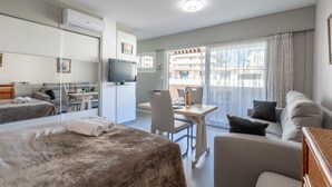 Una habitación de hotel moderna con una cama, un sofá, un escritorio con una silla, un televisor y un balcón con vistas a edificios.