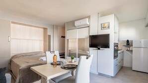 Habitación de hotel compacta con cama, una pequeña mesa de comedor, una silla, televisor, kitchenette y espejo.