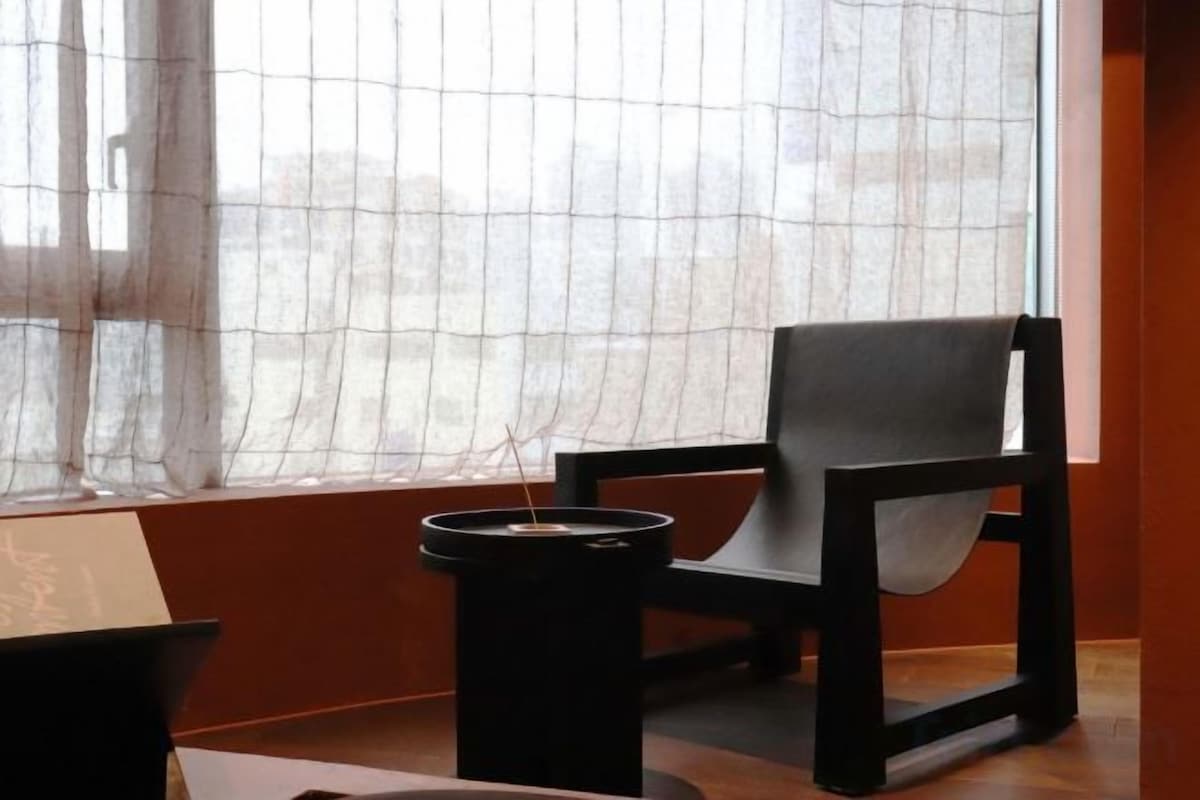 A room with a window, a chair, and a black trash bin.