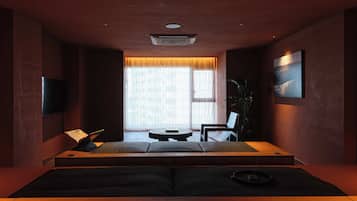 A modern room with a large window, a flat-screen TV, a sofa, a chair, and a small table.