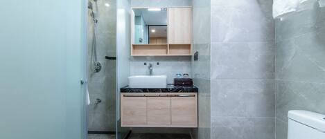 Un baño moderno con cabina de ducha de vidrio, lavamanos blanco y tocador de madera.