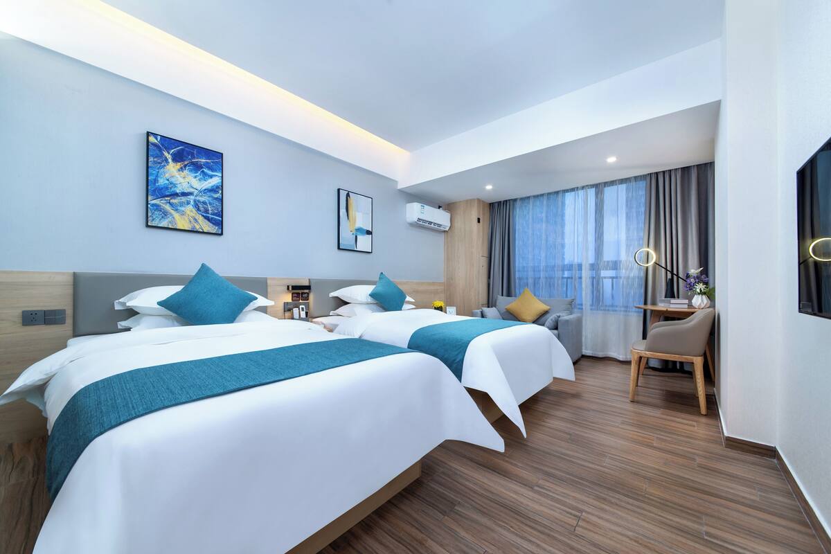Ein modernes Hotelzimmer mit zwei Betten, einem Schreibtisch und einem großen Fenster mit Vorhängen.