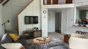Ett rymligt vardagsrum med en trappa, en platt-TV som är monterad på väggen, ett soffbord i trä och en soffa med kuddar.