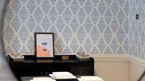 A room with a patterned wallpaper, a framed picture on the wall, and a table with plates and cutlery.