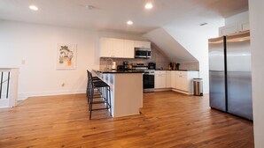 Une cuisine moderne avec des meubles blancs, un réfrigérateur en acier inoxydable et un plancher en bois.