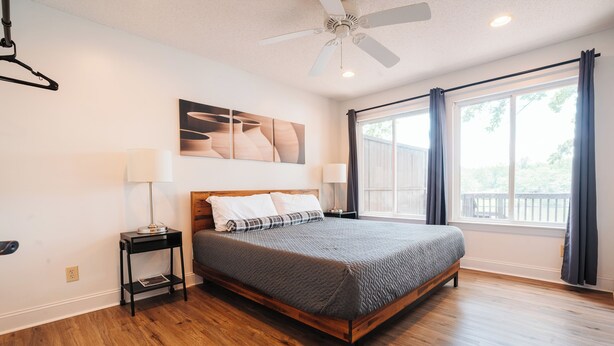 Une chambre à coucher avec un lit en bois, un ventilateur de plafond, une fenêtre avec des rideaux et une lampe fixée au mur.