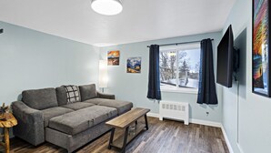 A living room with a sectional sofa, a wooden coffee table, a radiator, and a window with curtains. - 5 Min walk to restaurants/cafes, 8 min drive to airport, 10 min walk to trails. (Anchorage)