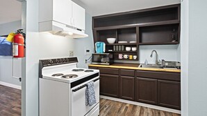 A compact kitchen with a white stove, dark wooden cabinets, and a microwave. - 5 Min walk to restaurants/cafes, 8 min drive to airport, 10 min walk to trails. (Anchorage)