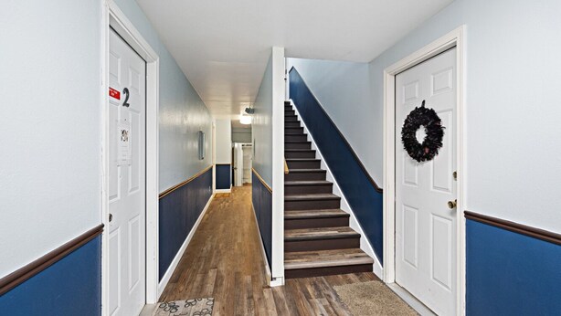A hallway with a wooden staircase, white doors, and a blue and white color scheme. - 5 Min walk to restaurants/cafes, 8 min drive to airport, 10 min walk to trails. (Anchorage)