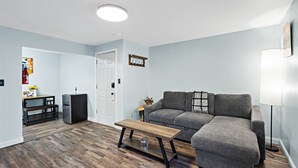 A living room with a grey sofa, a wooden coffee table, and a small side table. - 5 Min walk to restaurants/cafes, 8 min drive to airport, 10 min walk to trails. (Anchorage)